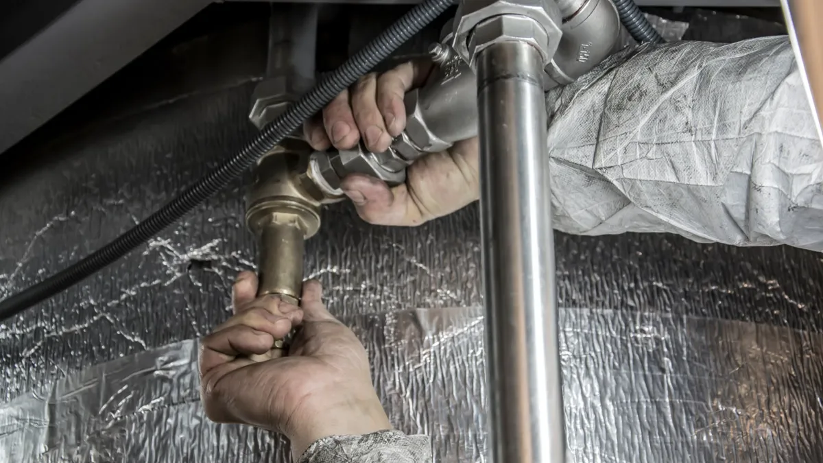 Hands fitting a new valve onto a water supply pipe under a house