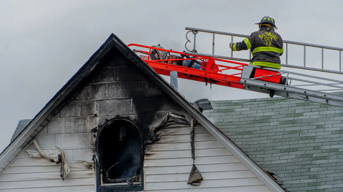 Firefighter on a ladder above the charred, smoke-stained gable of a house after a fire